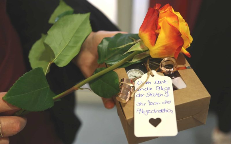 Eine gelb-orange Rose, an ihr ein Schild mit der Aufschrift "Vielen Dank an die Pflege der Station 0