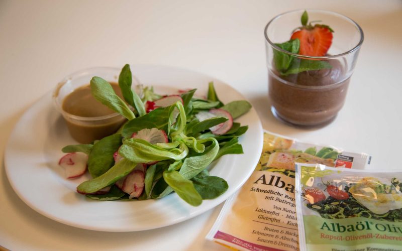 Ein grüner Salat mit Dressing, ein Schokoladen-Dessert mit Erdbeere und zwei Plastiktütchen mit der Aufschrift "Albaöl"